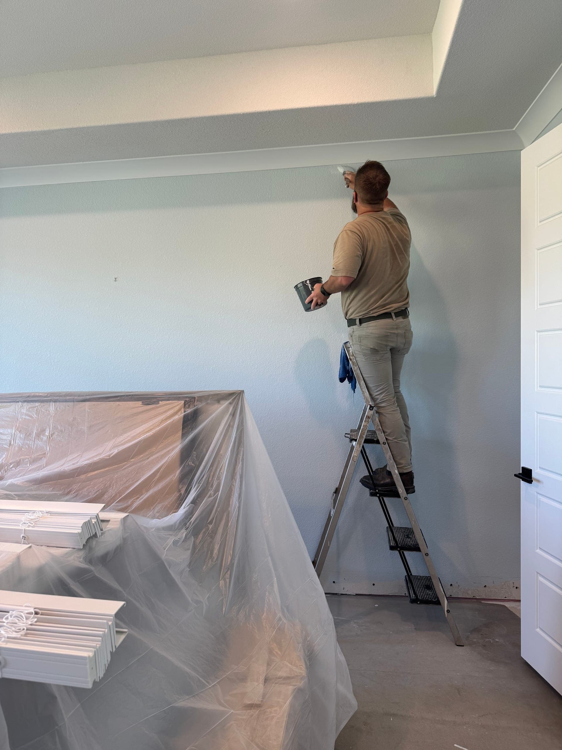 Chilton Home Services painting an interior wall with furniture covered and protected